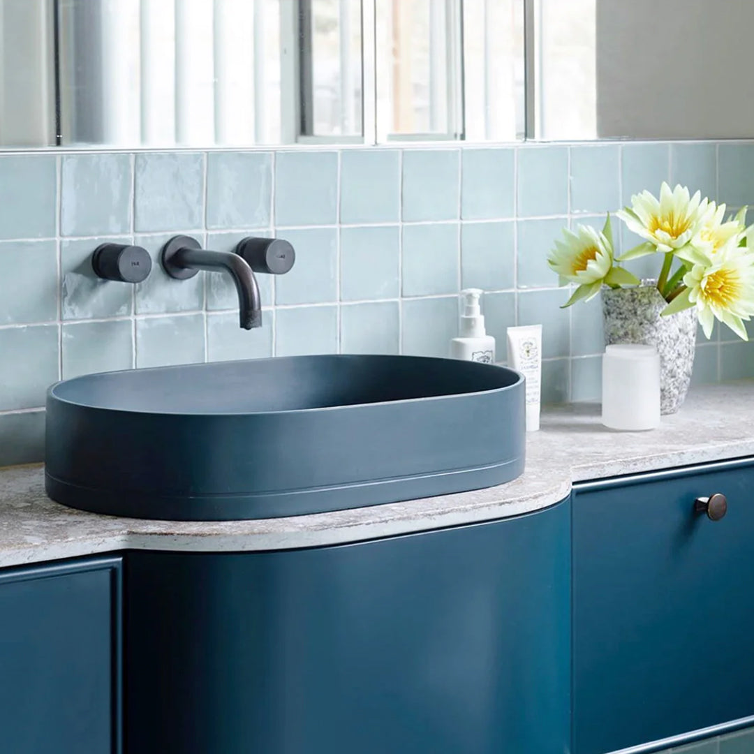 Bathroom vanity with blue sink and black faucet against a light blue tiled wall.