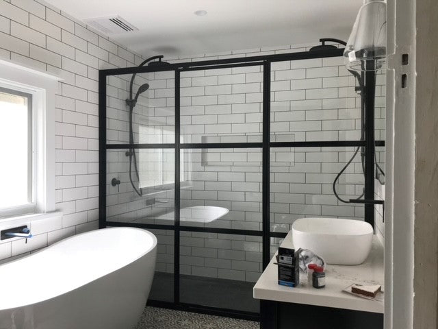 A fully framed shower screen with clear glass and a black frame installed in a bathroom, beside a bathtub and under a white tiled ceiling.